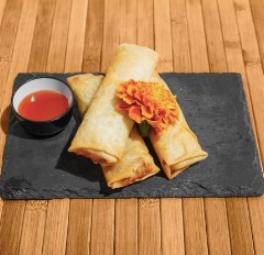 Tacos dorados servidos en una tabla de piedra, acompañados de salsa roja y decorados con una flor de cempasúchil.