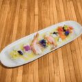 Plato de ceviche de camarones decorado con flores comestibles y servido sobre una base de madera. Ideal para amantes de la gastronomía gourmet.