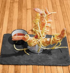 Camarones fritos decorados con fideos crujientes, servidos en una bandeja de piedra negra con salsa agridulce, ideales para un plato creativo en un restaurante.