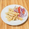 Plato de calamares fritos servido con rodajas de cebolla morada y tomate, sobre una mesa de madera.