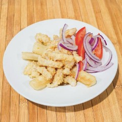 Plato de calamares fritos servido con rodajas de cebolla morada y tomate, sobre una mesa de madera.
